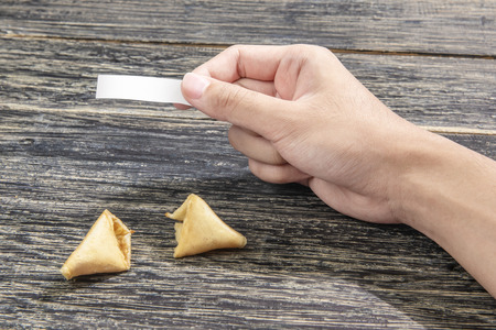 Human hand holding blank paper for quote or message from fortune cookies on wooden tableの写真素材