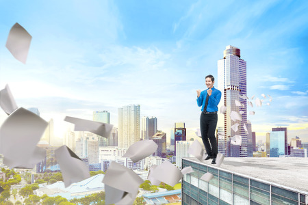 Handsome asian businessman standing with flying paper on the building rooftop in the cityの写真素材