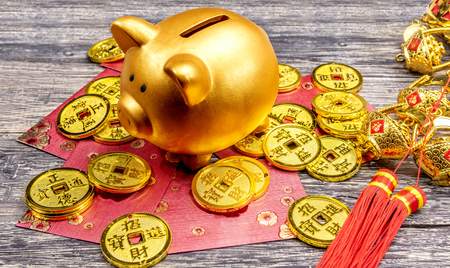 Piggy bank with golden coins, red envelopes and chinese ornament on the wooden table. Chinese New Year. Year of the earth pigの写真素材