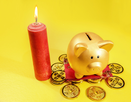 Piggy bank standing on golden coin and red envelopes with red candle over yellow background. Chinese New Year. Year of the earth pigの写真素材