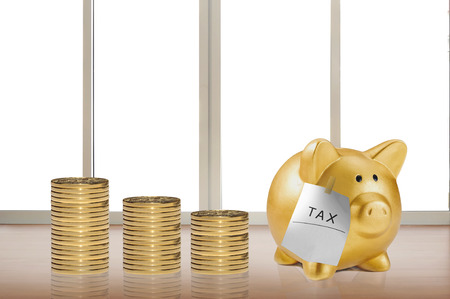 Stack of gold coins with taxes note on piggy bank. Taxes conceptの写真素材