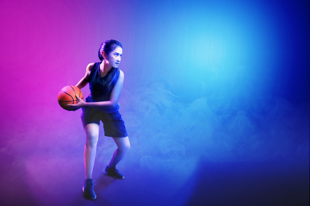 Young asian woman playing basketball against colorful backgroundの写真素材