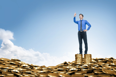 Attractive asian businessman standing on the top of coin stack. Business conceptの写真素材