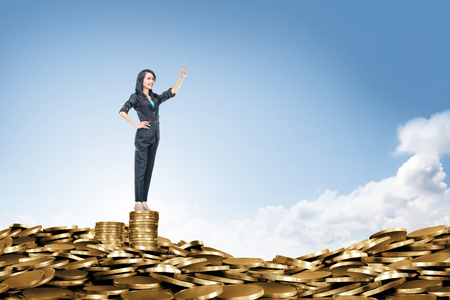 Happy asian business woman standing on the peak of coin pile. Business conceptの写真素材