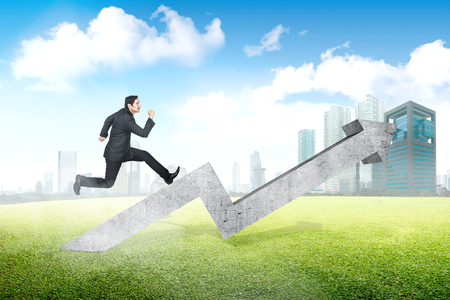 Young asian businessman running on increased chart with city backgroundの写真素材