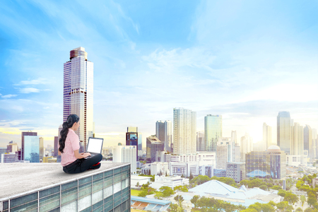 Back view of asian business woman working with laptop on the rooftopの写真素材