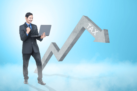 Happy asian businessman with laptop looking at declining tax graph arrow. Taxes conceptの写真素材
