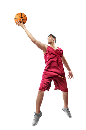 Attractive asian basketball player man in red uniform jumping with ball in hands isolated over white backgroundの写真素材