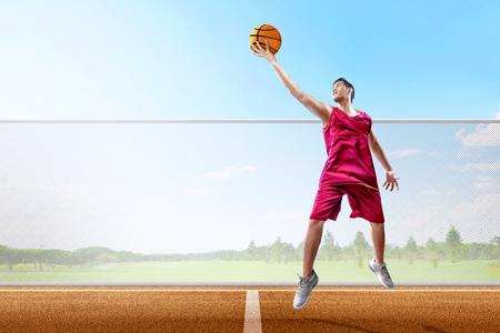 Excited asian basketball player man with ball in hand jumping high on the basketball courtの写真素材