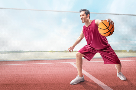 Cheerful asian basketball player man in action with the ball on the outdoor basketball courtの写真素材