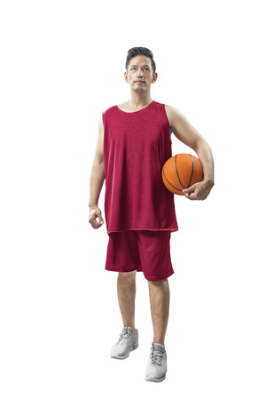 Portrait of asian sporty man with red uniform holding basketball standing isolated over white backgroundの写真素材