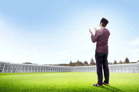 Back view of asian man standing on grass raise the hands and gazing the sky on the outside the mosqueの写真素材