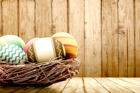 Colorful easter eggs in the nest on wooden table with wooden wall background. Happy Easterの写真素材