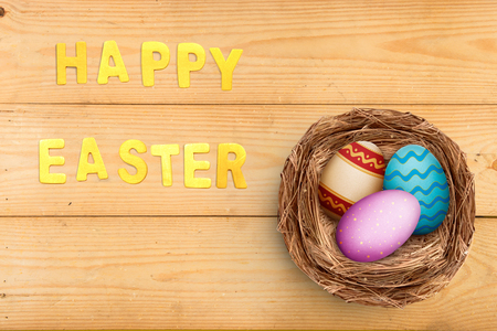 Colorful easter eggs in the nest on wooden table with happy easter greeting. Happy Easterの写真素材