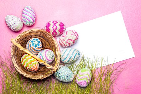 Colorful easter eggs in the nest and grass with blank white paper on the pink background. Happy Easterの写真素材