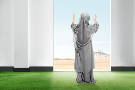 Rear view of asian little girl in veil standing on carpet raise the hand and gazing the sky from inside the room with open door and blue sky backgroundの写真素材