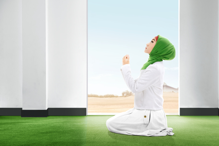 Pretty asian woman in veil sitting in praying position on the carpet rise the hands and looking up inside the room with open door and blue sky backgroundの写真素材