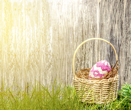 Colorful easter egg in the nest on wooden basket at the green grass with sunlight and wooden fence background. Happy Easterの写真素材