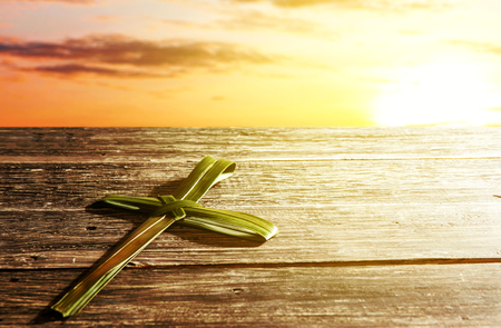 Cross shape of palm leaf on wooden table with rays of sunset background. Palm Sunday conceptの写真素材