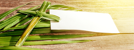 Closeup view of cross shape of palm leaf and palm branches with white blank paper and ray in wooden background. Palm Sunday conceptの写真素材