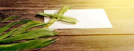Closeup view of cross shape of palm leaf and palm branches with white blank paper and ray in wooden background. Palm Sunday conceptの写真素材