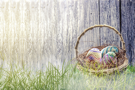Colorful easter eggs in the nest on wooden basket at green grass with  fog and wooden fence background. Happy Easterの写真素材