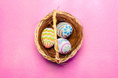 Colorful easter eggs on the nest in wooden basket on pink background. Happy Easterの写真素材