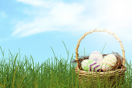 Colorful easter eggs on the nest in wooden basket on green grass with blue sky background. Happy Easterの写真素材