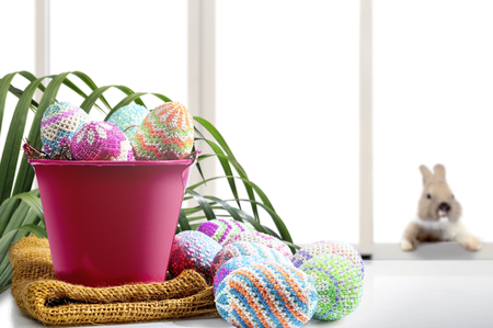 Colorful easter eggs on nest in the red bucket with fabric and table with palm branches and little bunny on window glass background. Happy Easterの写真素材