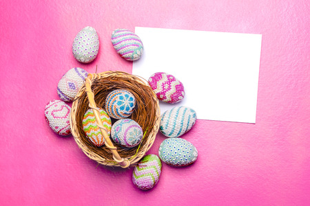 Colorful easter eggs on the nest in wooden basket with blank white paper on the pink background. Happy Easterの写真素材