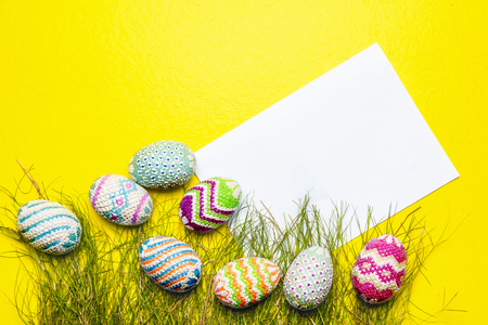 Colorful easter eggs with grass and blank white paper on yellow background. Happy Easterの写真素材