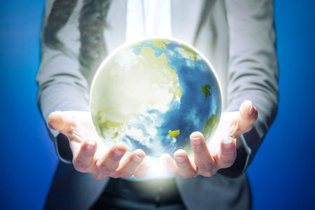Business woman standing with open palm holding the earth with both hands over blue background. Earth day conceptの写真素材