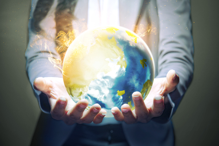 Business woman standing with open palm holding the earth with fire effect using her both hands over dark background. Earth day conceptの写真素材