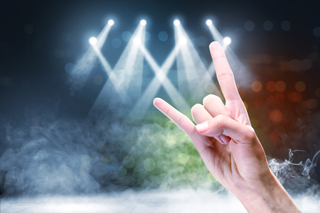 Close up view of man hand with rock gesture sign against concert spot lighting and smoke with defocused colorful lights backgroundの写真素材