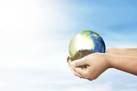 Hands holding soil with earth planet over blue sky background. Earth hour conceptの写真素材