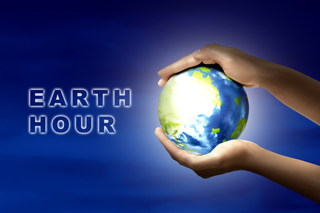 Hands holding earth planet with earth hour message over night background. Earth hour conceptの写真素材