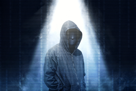 Hacker in black hoodie standing with smoke and light from the top over dark backgroundの写真素材