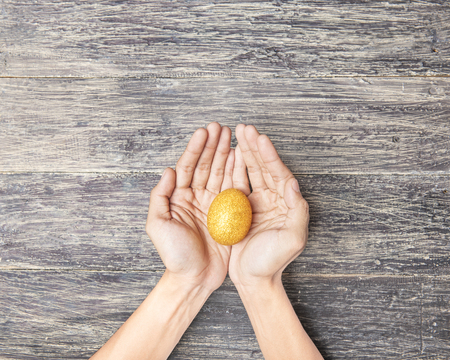 Human hands holding yellow easter egg over wooden table background. Happy Easterの写真素材