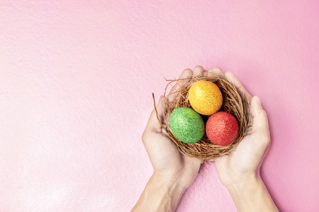 Human hands holding the nest with colorful easter eggs over pink color background. Happy Easterの写真素材