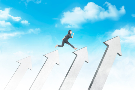 Happy asian business woman jumping above white arrows with blue sky background. Business conceptの写真素材