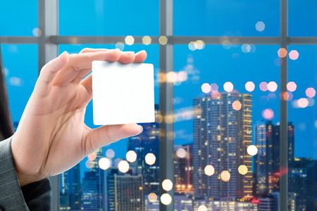Business woman hand showing white blank card on the office with city at night background. White blank card for copyspaceの写真素材