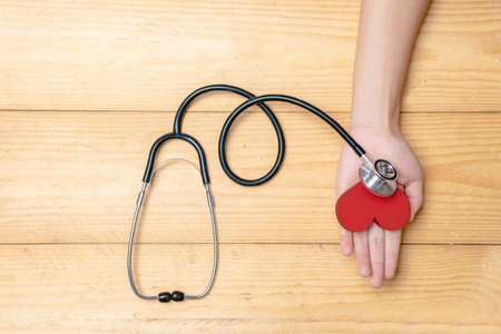 Human hand holding red heart and stethoscope over wooden table background. Health day conceptの写真素材