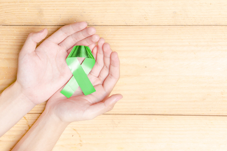 Human hands showing green ribbon over wooden table background. Health day conceptの写真素材