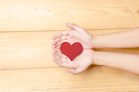 Human hands holding red heart over wooden table background. Health day conceptの写真素材