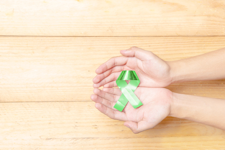 Human hands showing green ribbon over wooden table background. Health day conceptの写真素材