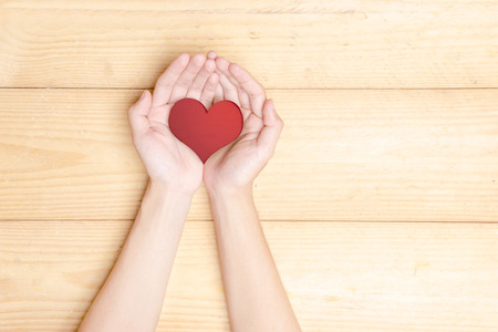 Human hands holding red heart over wooden table background. Health day conceptの写真素材
