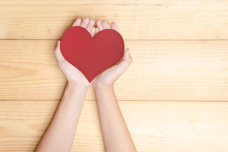 Human hands holding red heart over wooden table background. Health day conceptの写真素材
