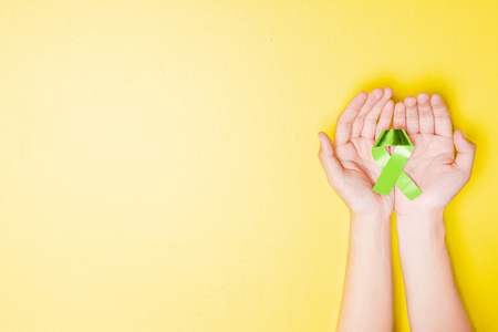 Human hands showing green ribbon over yellow color background. Health day conceptの写真素材