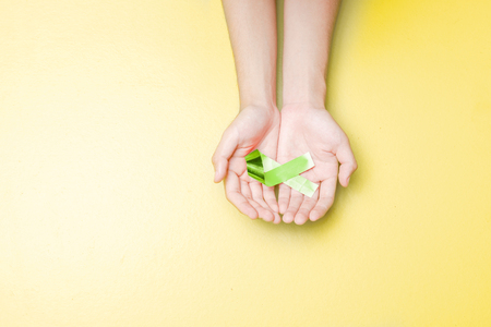 Human hands showing green ribbon over yellow color background. Health day conceptの写真素材