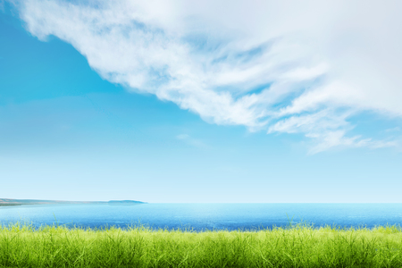 Green grass with blue ocean view and cloudscapes over blue sky backgroundの写真素材